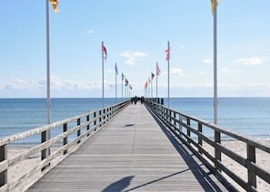 A wooden pier extending into the sea with flags on both sides, leading to a sandy beach. - House El Mar, Apartment H "beachlove" (Grossenbrode)