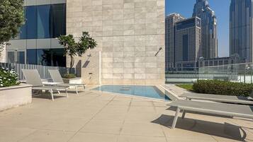 A rooftop pool area with lounge chairs and a view of tall buildings.