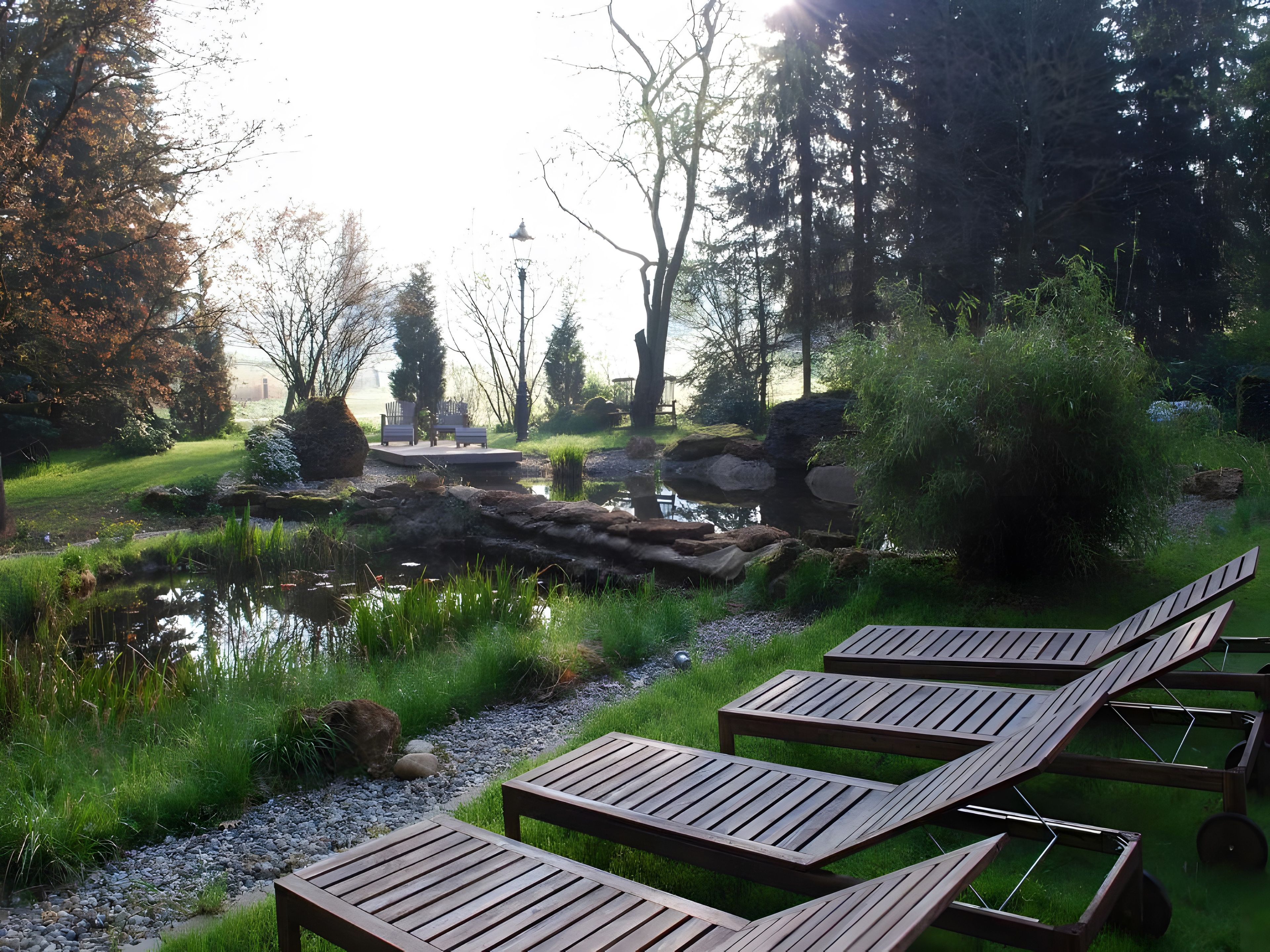 A serene outdoor area with a pond, wooden lounge chairs, and a seating area with benches.
