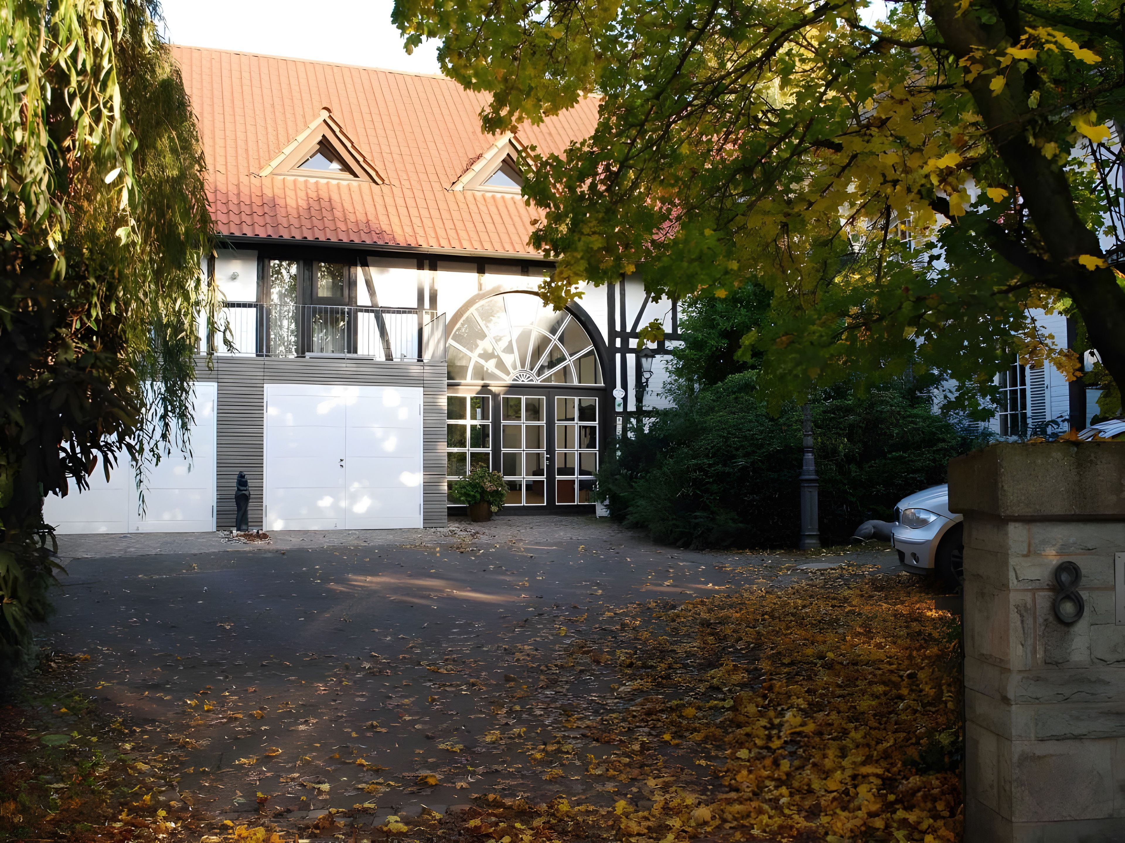 A building with a large arched window, a garage, and a driveway with fallen leaves.