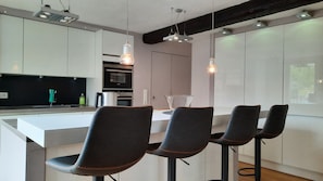 Una cocina moderna con una isla central, taburetes de bar, iluminación colgante y electrodomésticos integrados.
