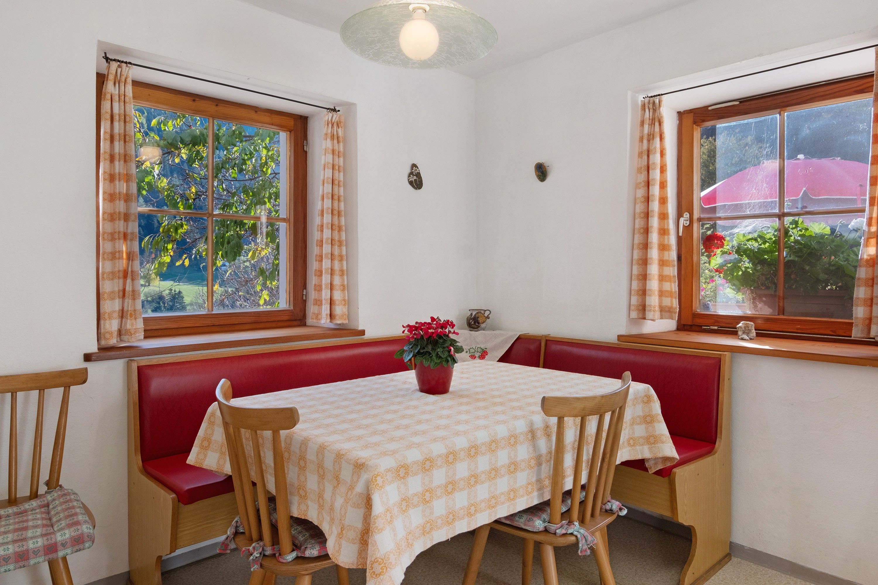 A dining area with a table set for two, red cushioned benches, and a potted plant on the table.