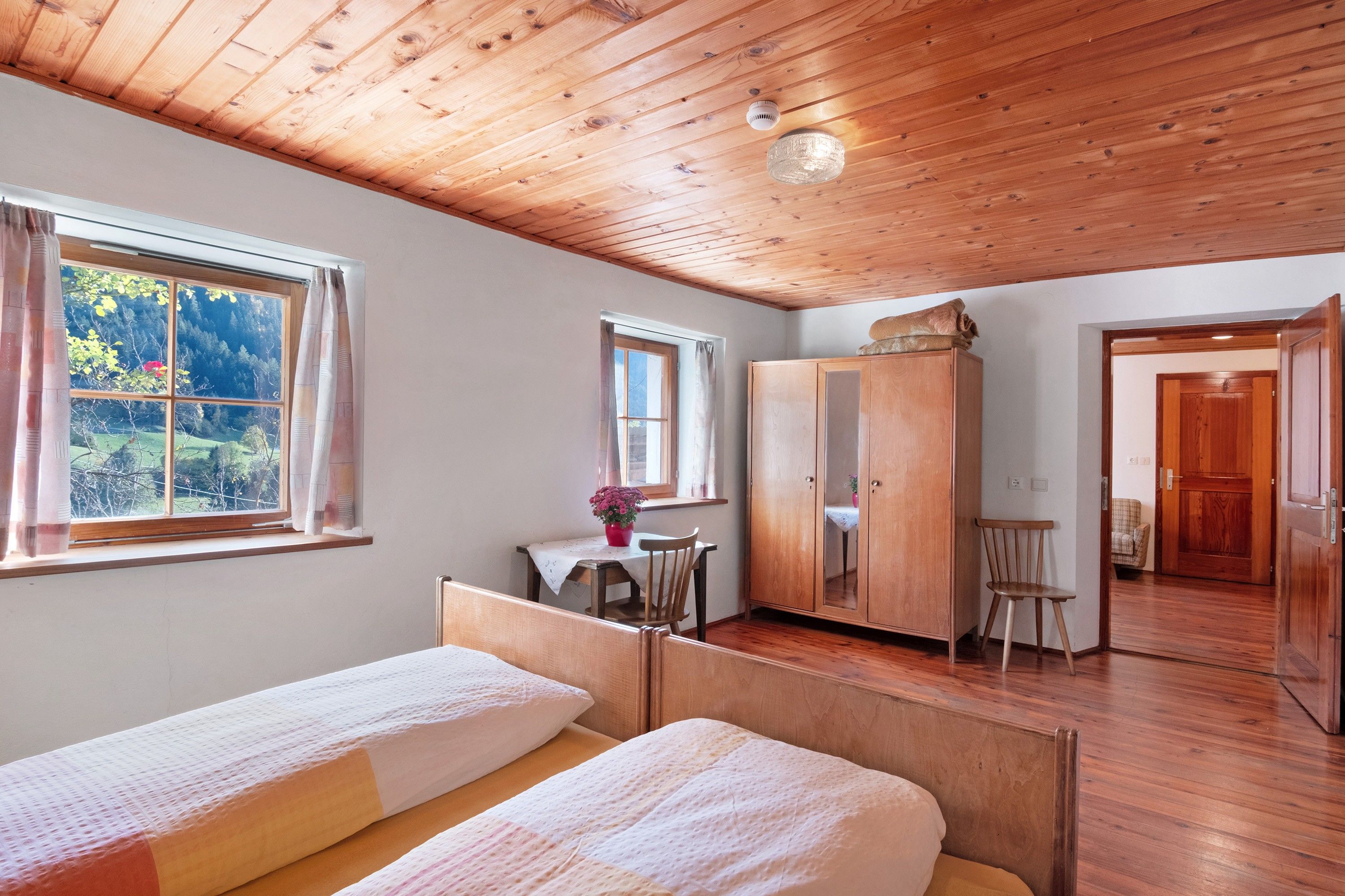 Ein Zimmer mit Holzboden, einem Bett, einem Schreibtisch, einem Stuhl und einem Kleiderschrank.