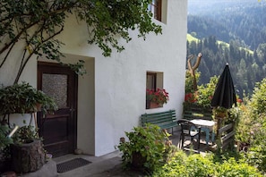 A white building with a door, a window with flowers, a bench, a table with a chair, and an umbrella. - Apartment 'Rosengarten Mitterbirbach' with Mountain View, Private Terrace and Wi-Fi (Sankt Pankraz)
