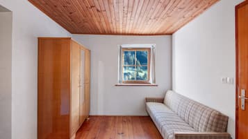 A room with a wooden ceiling, a window with a view of trees, a wooden wardrobe, and a sofa.