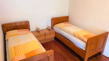 Ein Zimmer mit zwei Holzbetten, einem Nachttisch mit Lampe und Holzboden.