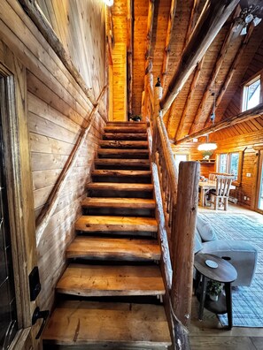 Eine Holztreppe führt zu einem Raum mit Tisch und Stühlen, einem Fenster und einem Deckenventilator.