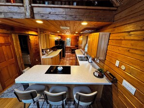 A kitchen with wooden walls, a central island with bar stools, and a view of the living area. - Wake up on the water at this 3-bedroom log cabin on Bergland Bay, Lake Gogebic. (Bergland)