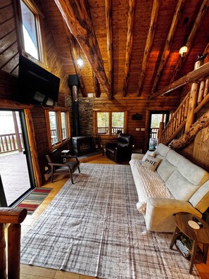 A log cabin interior with a fireplace, sofa, and wooden beams. - Wake up on the water at this 3-bedroom log cabin on Bergland Bay, Lake Gogebic. (Bergland)