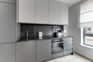 Una cocina moderna con armarios grises, horno empotrado y ventana con persianas.