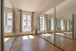 A spacious room with large windows, a herringbone wooden floor, and a mirrored wall. - Prestige Tr Moille Luxury 3bdr in the 8th Arron (Paris)