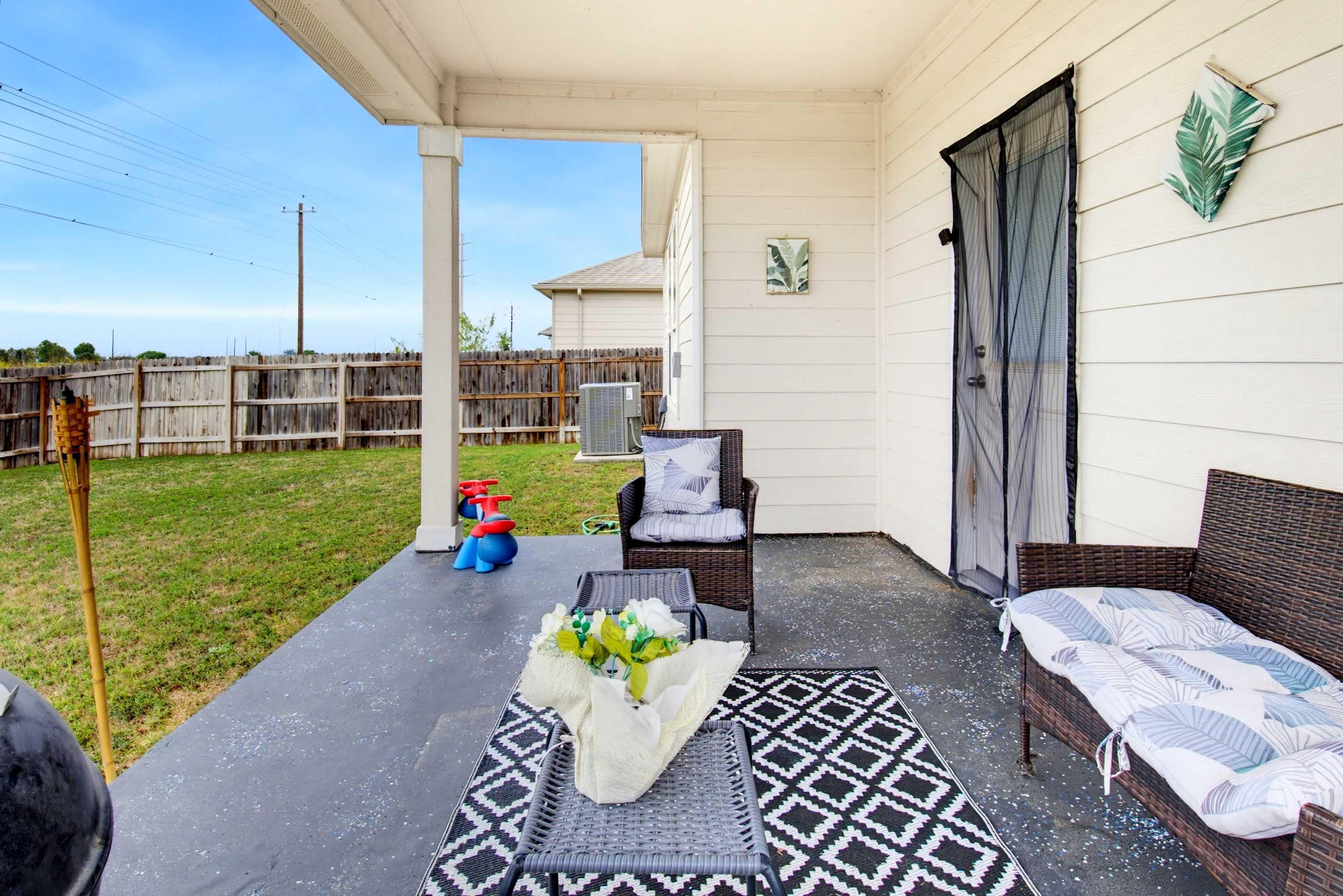 A covered patio area with outdoor furniture, a grill, and a fenced yard.