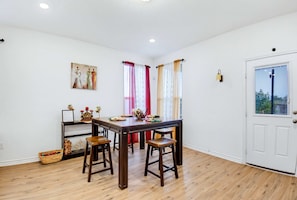 A dining area with a wooden table, four chairs, a small side table with decorative items, and a white door with a window. - Game Night HQ Arcade Pool Table 5BR (Seguin)