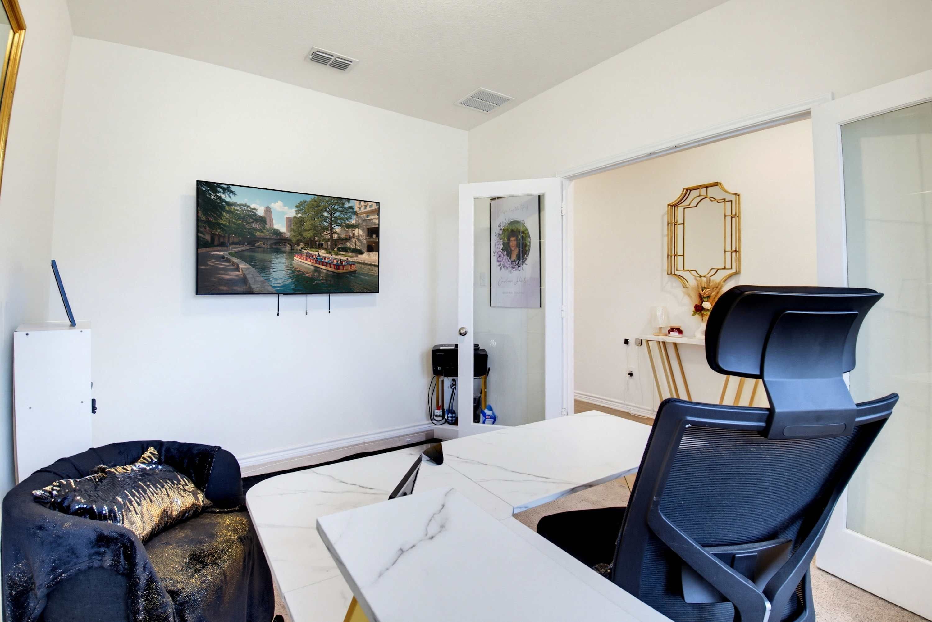A modern room with a white desk, a black chair, a sofa with a sequined cover, a television mounted on the wall, and a decorative mirror.