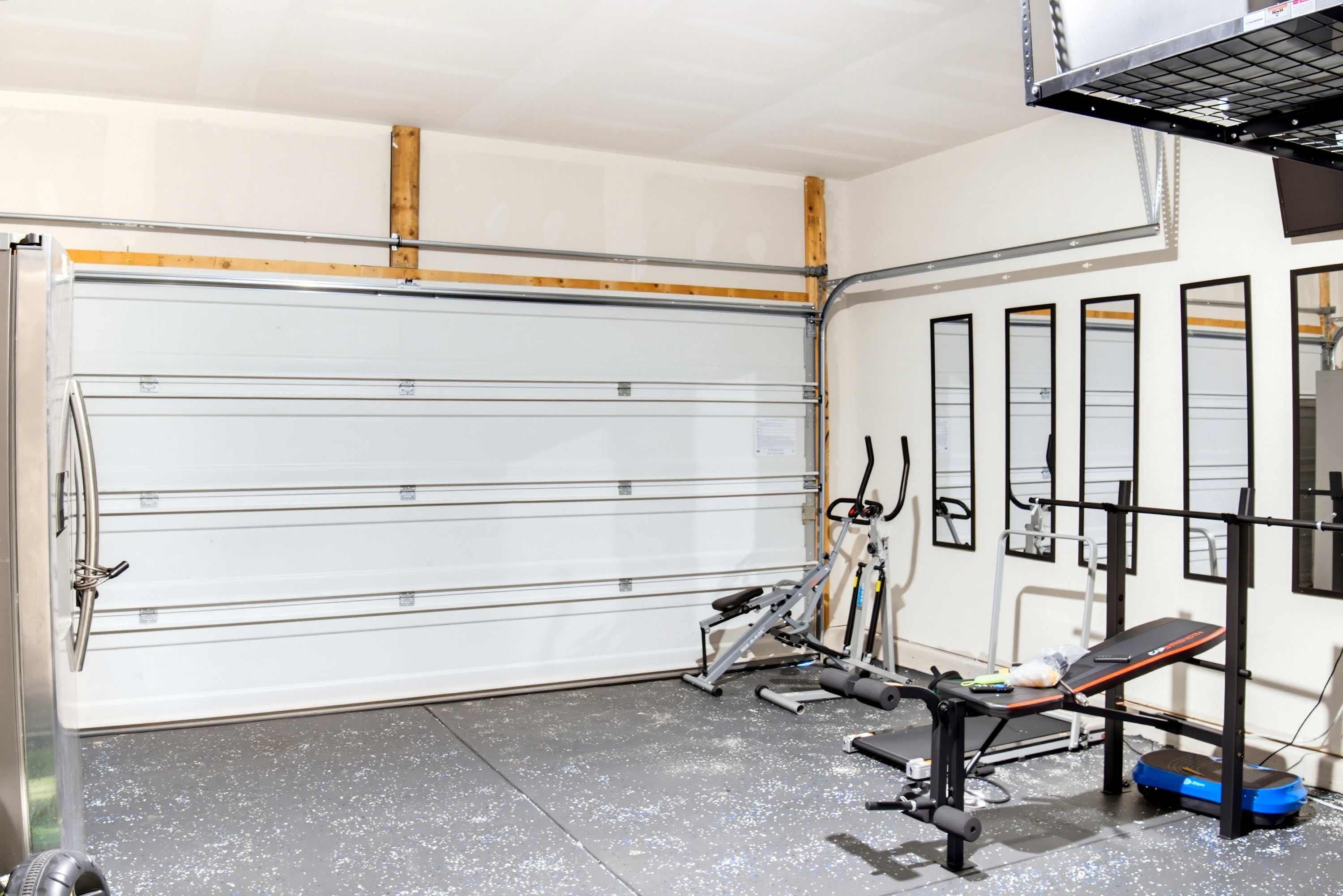 A garage with a closed garage door, exercise equipment, and a bench.
