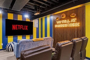 A room with a large flat-screen TV displaying 'NETFLIX', a neon sign reading 'WE YELL AT SCREENS HERE', and a couch with bean bags. - Indy Escape Sauna Hot Tub Firepit Games (South Bend)