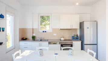 A modern kitchen with white cabinetry, a dining table with chairs, and a refrigerator.