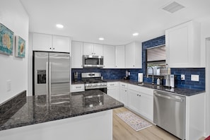 Et moderne køkken med hvide skabe, rustfrie hvidevarer og et backsplash med blå fliser.