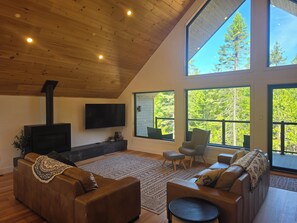 A modern living room with a fireplace, large windows, and a high ceiling. - La Tanière de l'Ours BJÖRN HÎ, Refuge & Réconfort (Saint-Côme)