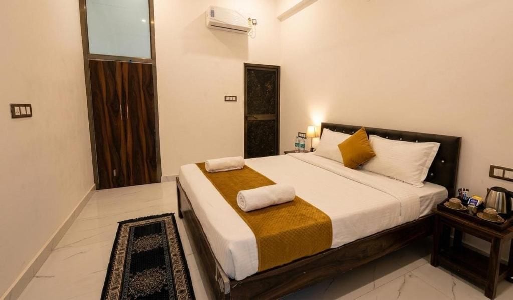 A hotel room with a bed, a nightstand, a wall-mounted air conditioner, and a door with a wooden panel.
