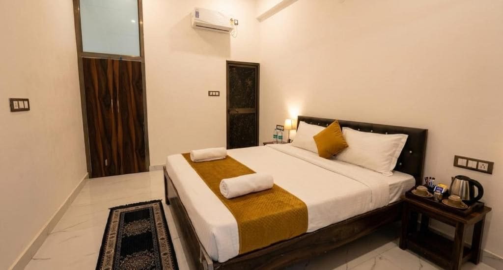 A hotel room with a bed, a nightstand, a wall-mounted air conditioner, and a door.