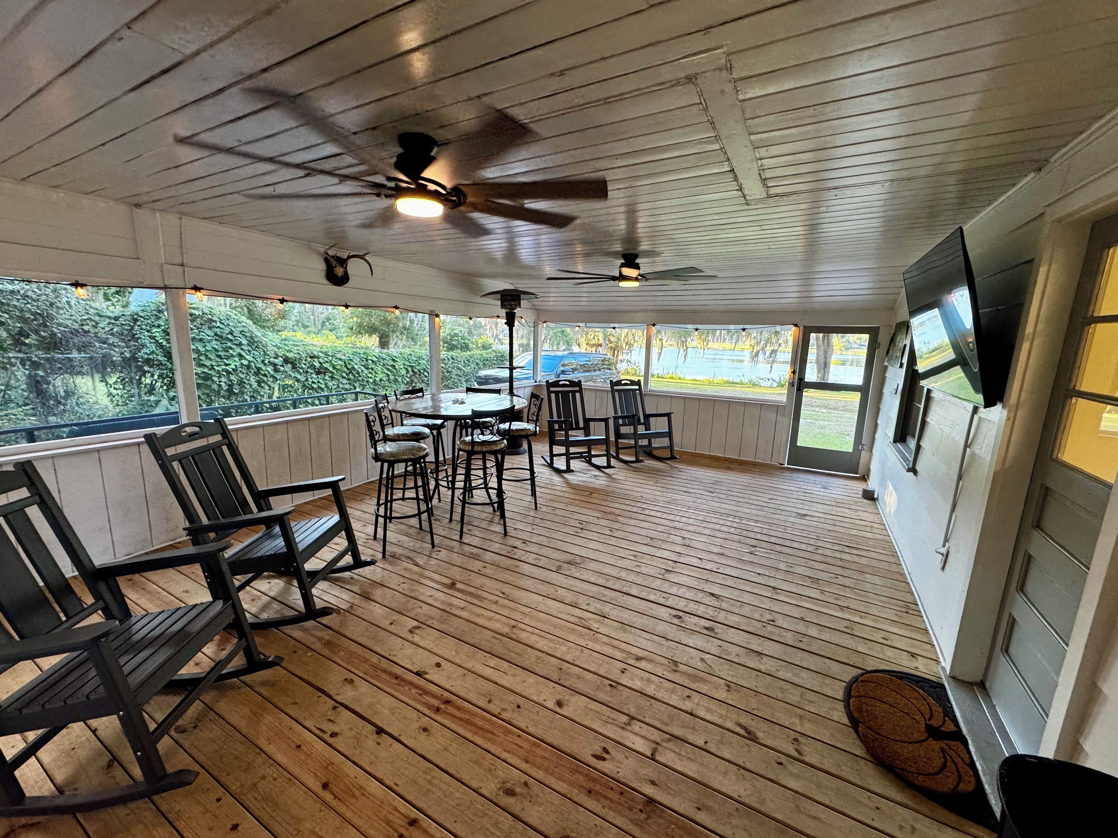 Ein überdachter Außenbereich mit Holzboden, Deckenventilatoren und einem Tisch mit Stühlen.