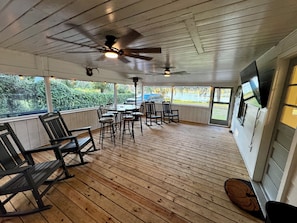 Ein überdachter Außenbereich mit Holzboden, Deckenventilatoren und einem Tisch mit Stühlen.