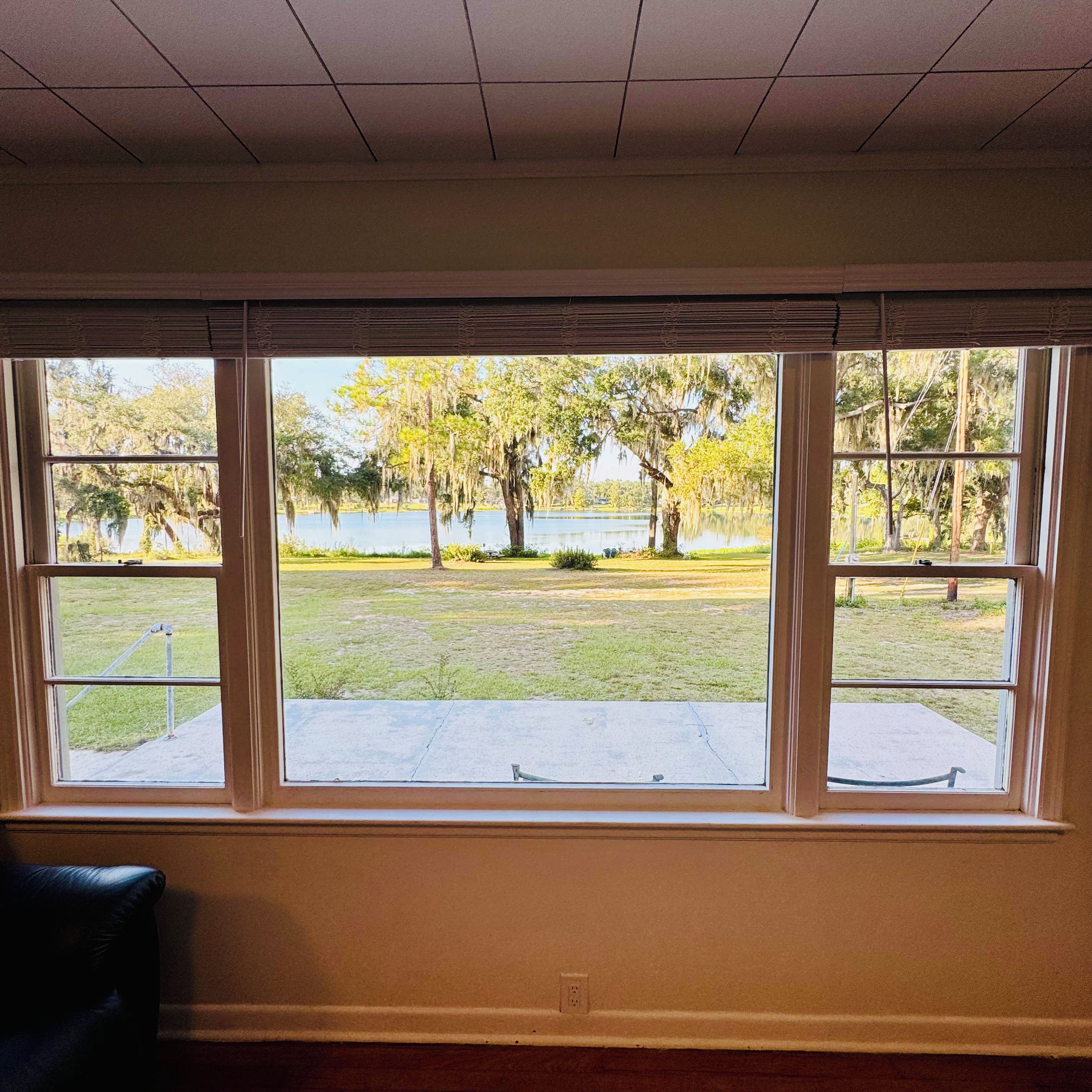 A room with a large window overlooking a grassy area with trees and a body of water.