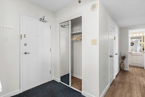 Ein Flur mit Teppichboden, ein Kleiderschrank mit Kleidung und ein Badezimmer mit Spiegel und Waschbecken.