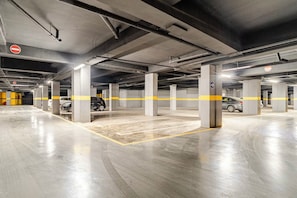 A multi-level parking garage with concrete pillars, yellow safety lines, and directional signs. - Dar Oud | Appartement 2 ch : Piscines, Jacuzzi, Gym & Parking - Marrakech (Marrakech)