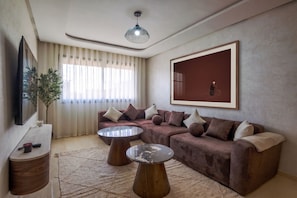 A modern living room with a sectional sofa, two coffee tables, a mounted TV, and a large framed artwork on the wall. - Dar Oud | Appartement 2 ch : Piscines, Jacuzzi, Gym & Parking - Marrakech (Marrakech)