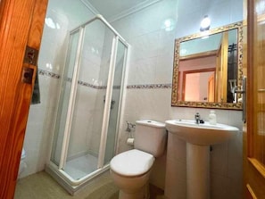 Et badeværelse med brusekabine i glas, toilet og vask med spejl over.