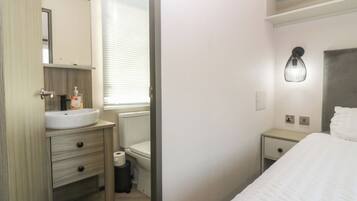 A hotel room with a bed, a bedside table, a nightstand, a bathroom with a sink, toilet, and a mirror.