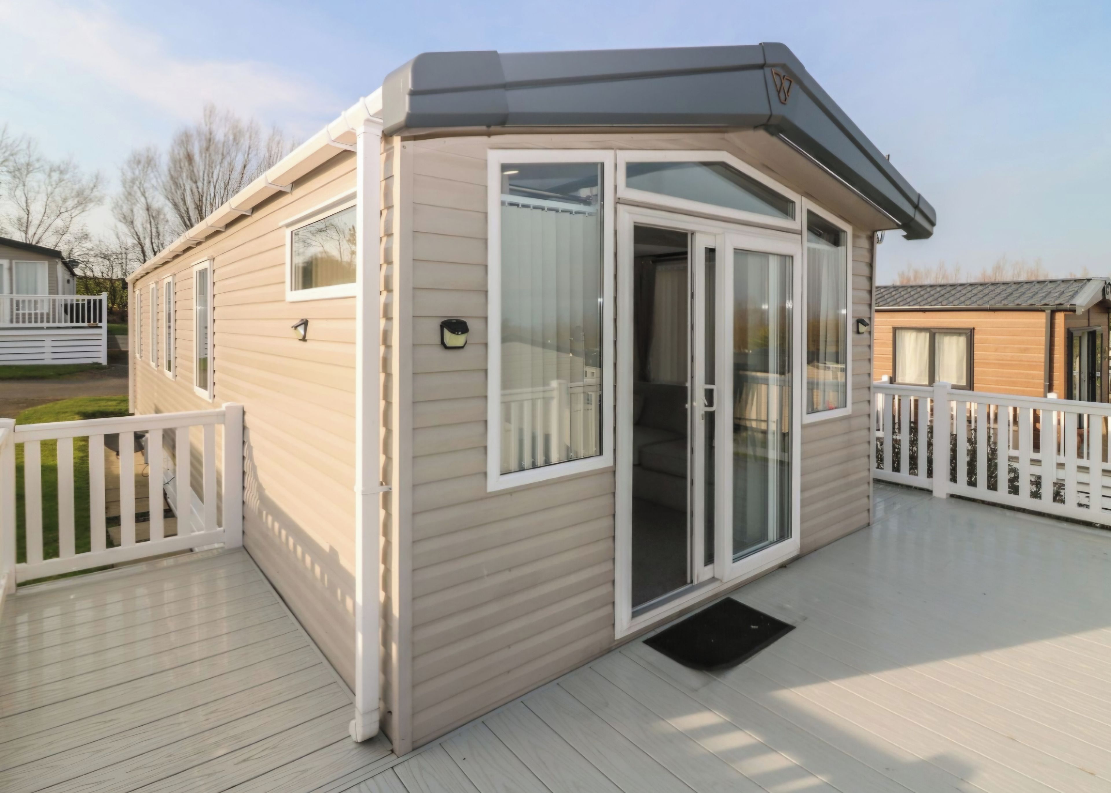 A single-story mobile home with a deck, white railings, and a sliding glass door.