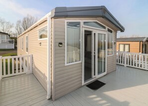 A single-story mobile home with a deck, white railings, and a sliding glass door. - Cabin Sleeps 6 With Parking (Eyemouth)
