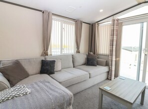 A living room with a sofa, a coffee table, and curtains. - Cabin Sleeps 6 With Parking (Eyemouth)