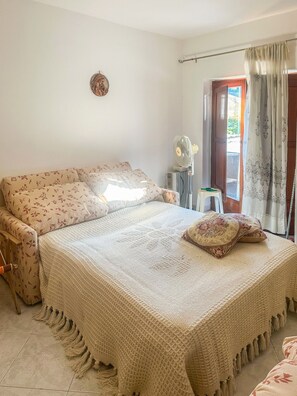 Une chambre avec un grand lit, une table de chevet, un ventilateur et une vue sur l’extérieur par une porte.