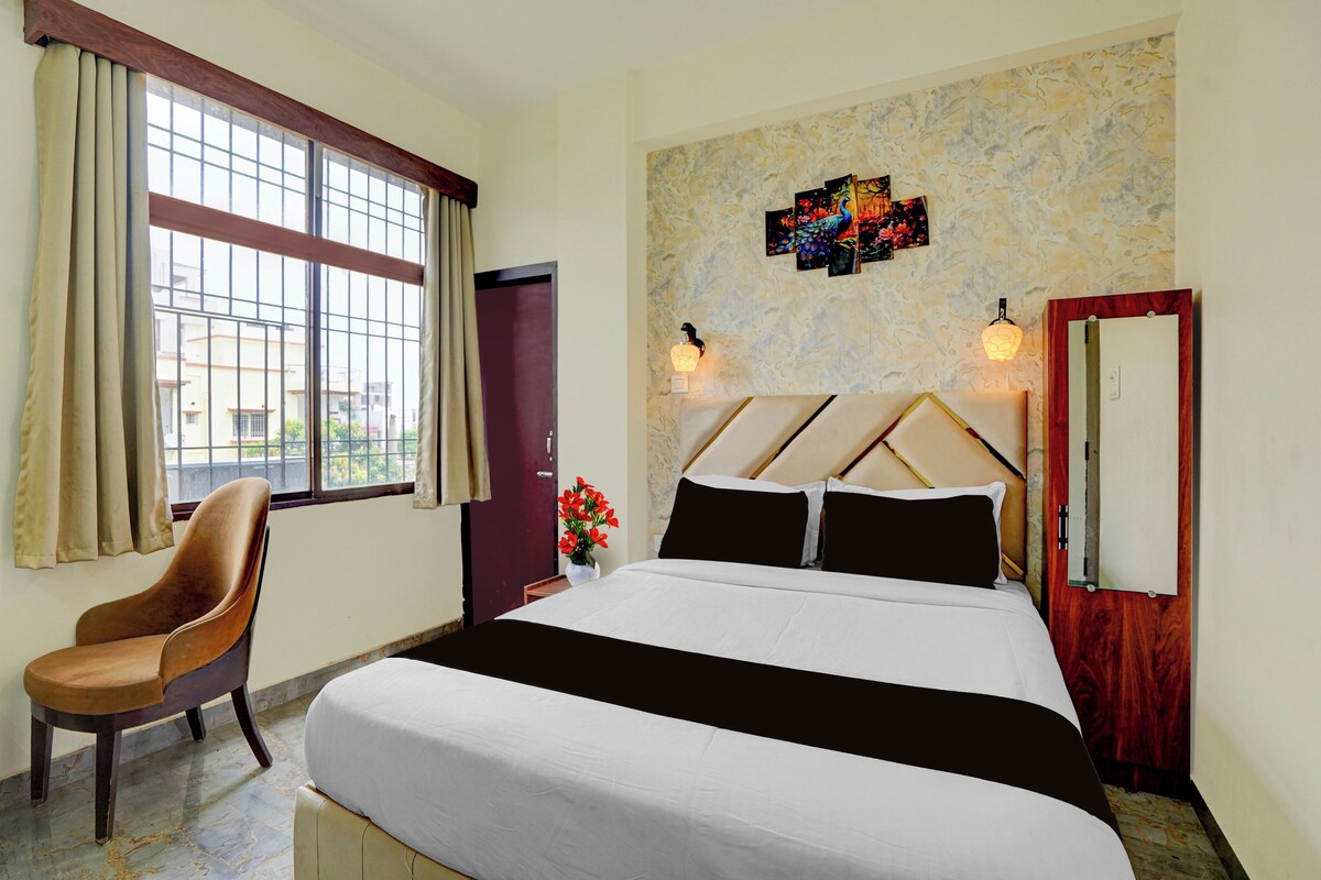 Habitación de hotel con cama, una silla, ventana con cortinas, una obra de arte en la pared y una puerta.