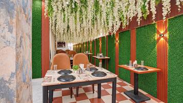 Interior de restaurante con suelo a cuadros, mesas dispuestas con platos, vasos y cubiertos, y un arreglo floral colgante.
