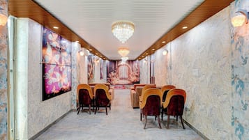 Un hall de hotel con suelo de mármol, techo de paneles de madera y una araña. Hay varias sillas y un mostrador de recepción.
