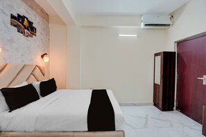 Habitación de hotel con cama, armario, equipo de aire acondicionado y una obra de arte colgada en la pared.