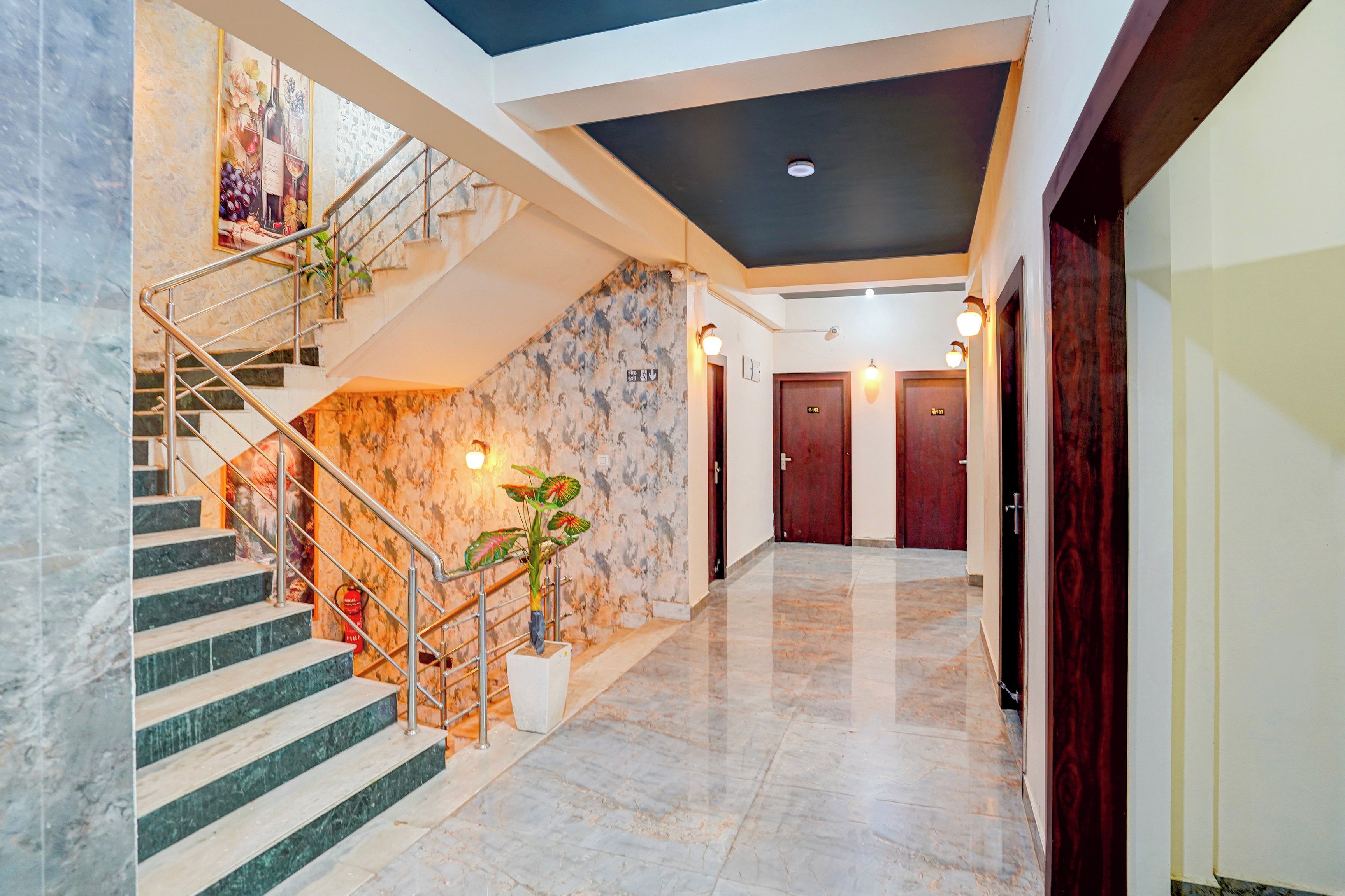 A hotel interior with a marble staircase, a wall-mounted plant, and a hallway leading to a door.