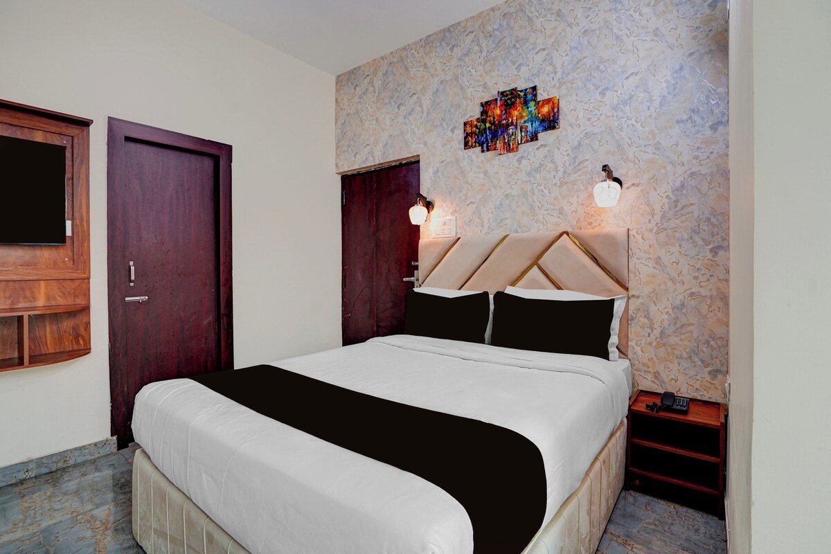 Habitación de hotel con cama, puerta de madera, pared con textura y una pequeña mesa con teléfono y lámpara.