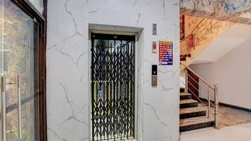 Un ascenseur doté d’une porte en métal noir, d’une alarme incendie et d’un escalier muni d’un tuyau d’incendie rouge.