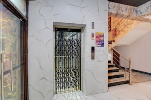 Un ascensor con una puerta metálica negra, un detector de incendios y una escalera con una manguera contra incendios roja.