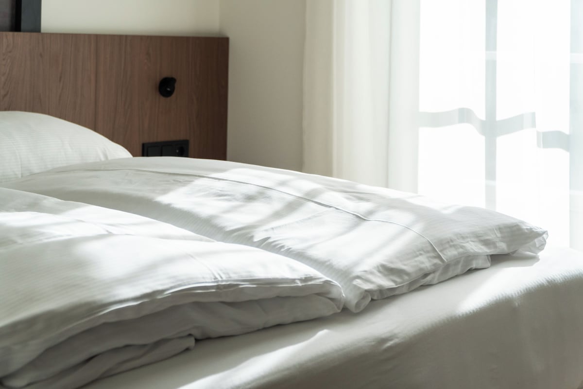 A neatly made bed with white linens in a hotel room.