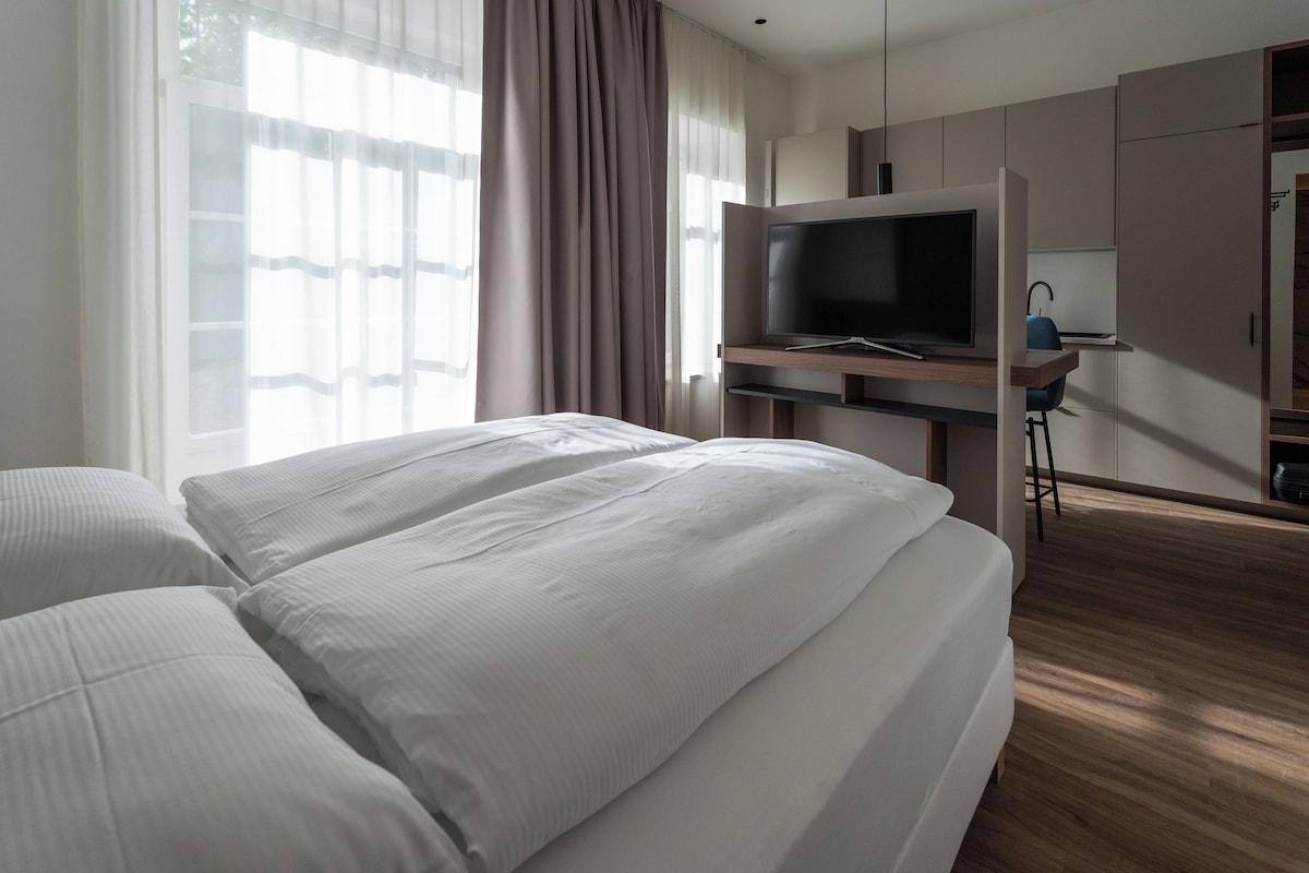 A hotel room with a bed, a television on a stand, and a desk with a chair.
