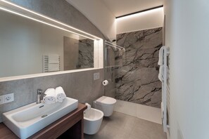 A modern bathroom with a large mirror, a sink, a toilet, and a shower area. - Aparthotel Krone 1895 (Klausen)