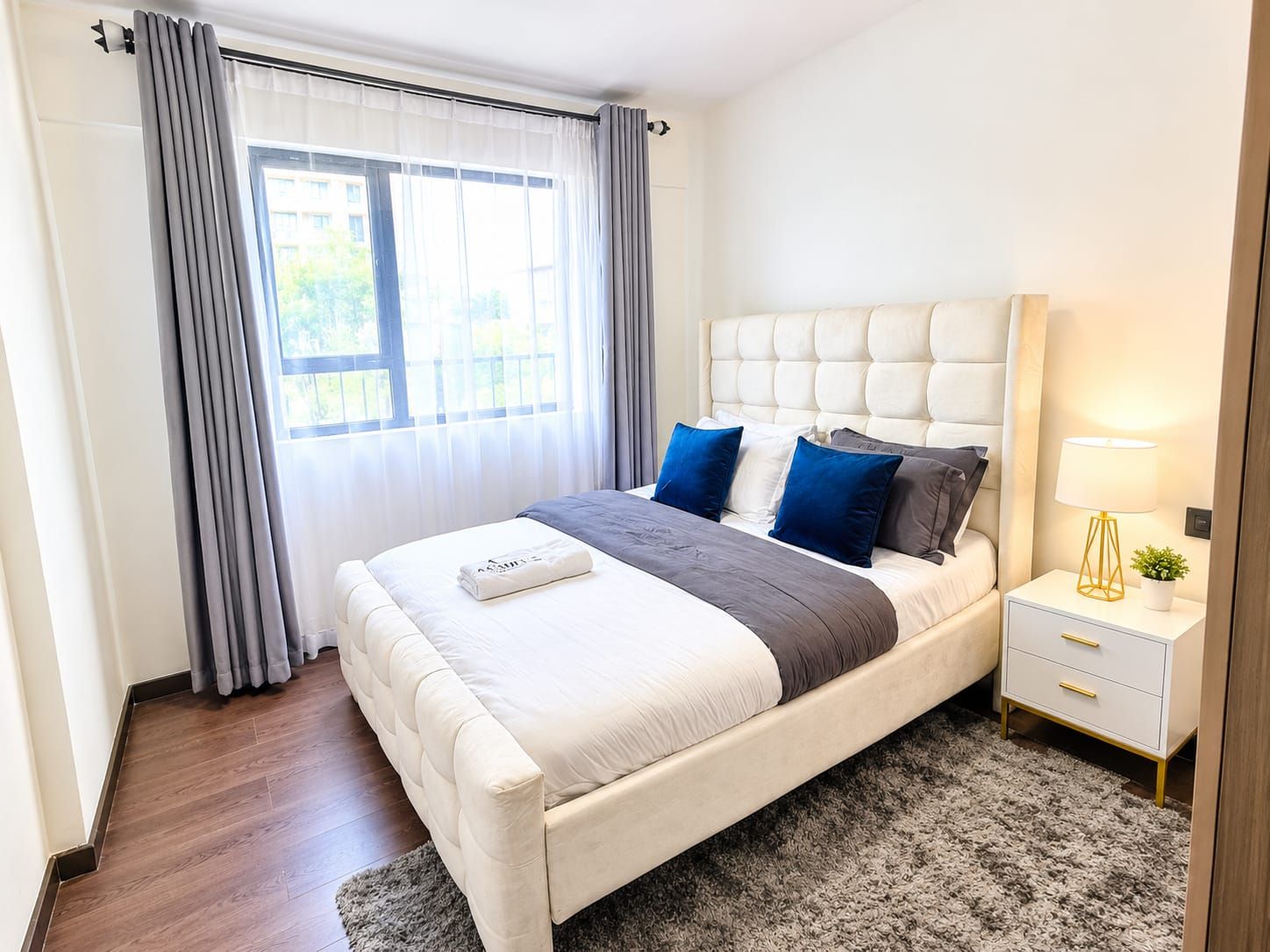 A modern bedroom with a bed, bedside tables, and a view of the outdoors.