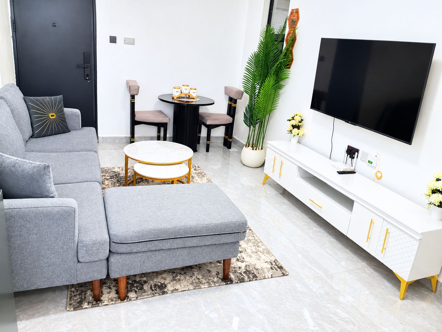 A modern living room with a grey sofa, a round coffee table, a white TV stand, and a potted plant.